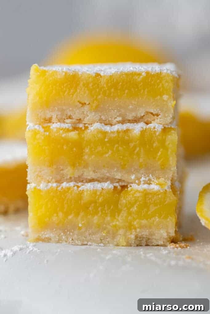Three squares from the easy lemon bars recipe stacked on top of each other, dusted with powdered sugar.