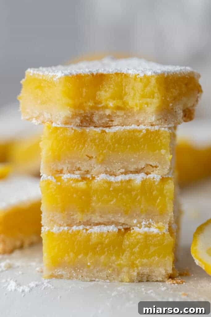 Four squares of the easy lemon bars recipe stacked on top of each other, displaying the thick lemon filling.