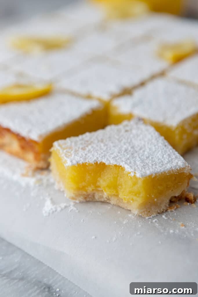 Fully baked easy lemon bars recipe cut into squares with a bite taken out, showing the texture of the filling and crust.
