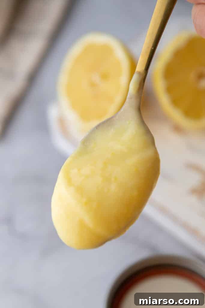 Microwave Magic: Luscious Lemon Curd in Minutes 4 A spoon dipping into creamy microwave lemon curd, showing its thick and glossy texture.