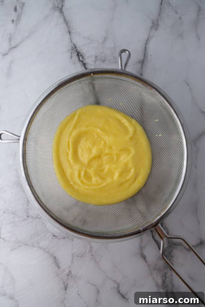 Microwave Magic: Luscious Lemon Curd in Minutes 8 Lemon curd being strained through a fine-mesh sieve to remove any lumps or zest.