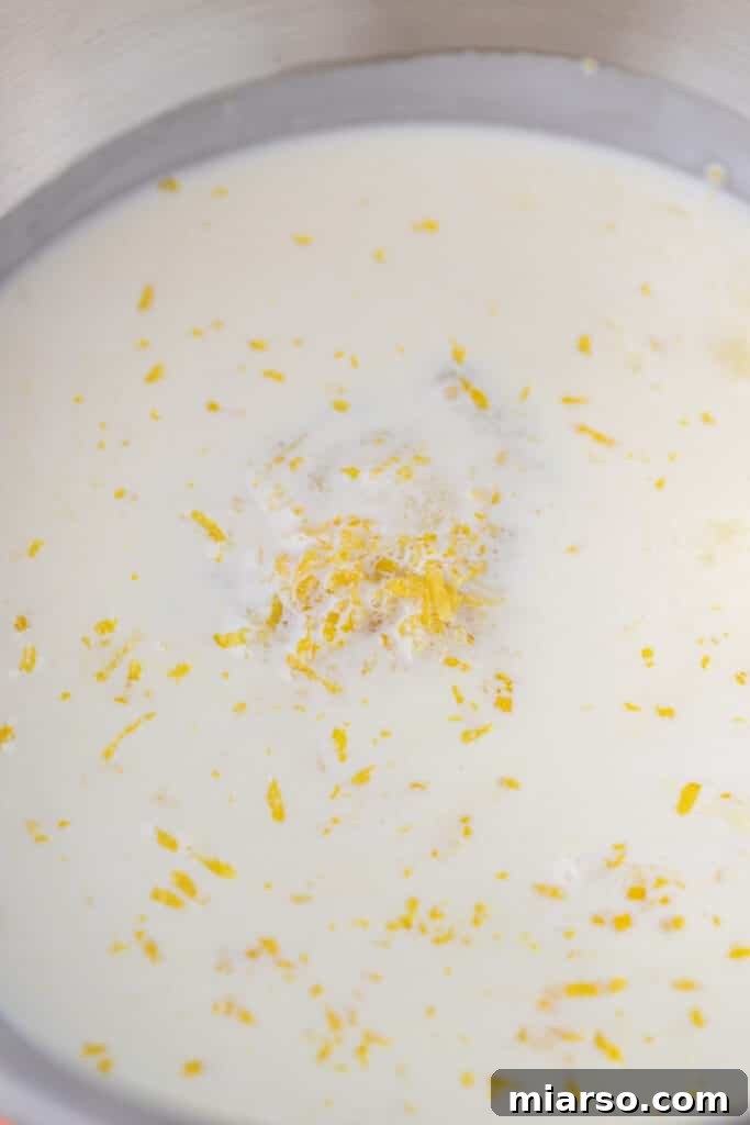 Unmixed ingredients for lemon posset in a small pot, including heavy cream, sugar, and lemon zest.