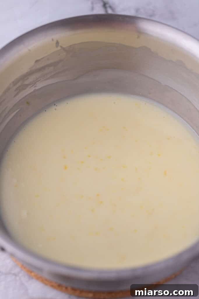Mixed ingredients for lemon posset simmering gently in a small pot on the stovetop.