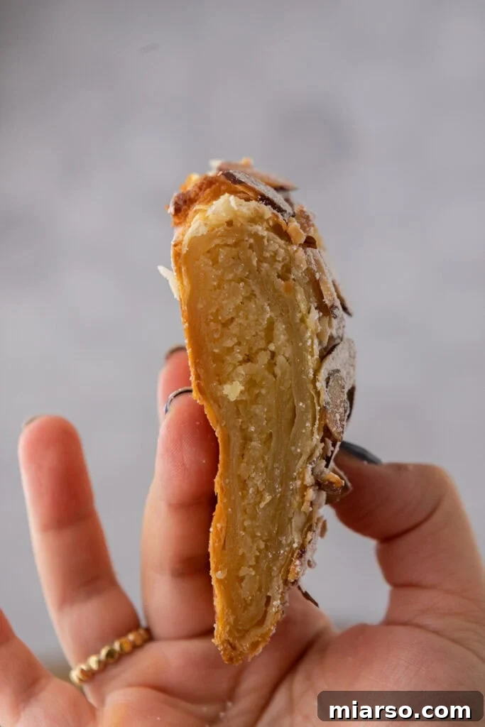 A single piece of braided almond croissant danish held by a hand, showing its flaky layers