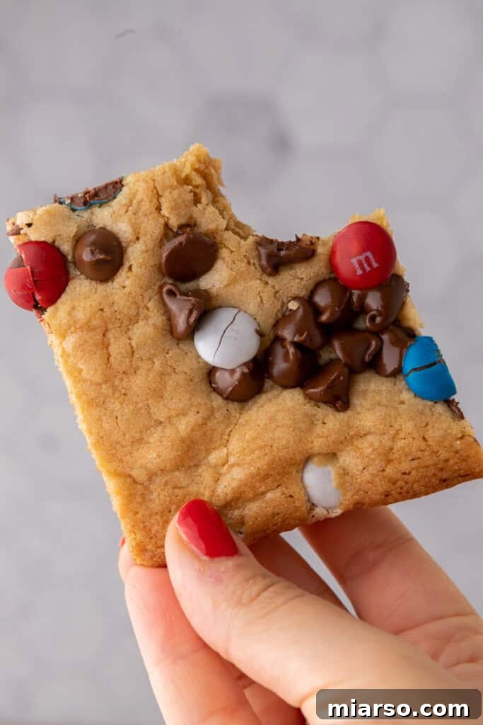Hand holding patriotic sheet pan red white and blue M&M's cookie bars, showcasing the vibrant colors and chewy texture.