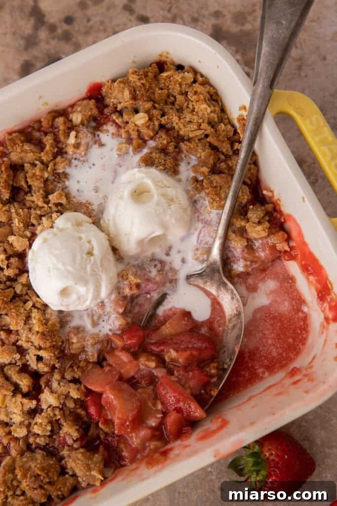 Your New Favorite Strawberry Rhubarb Crisp 12 Strawberry Rhubarb Crisp in a baking dish with a serving spoon, showing the gooey fruit filling and crunchy topping.