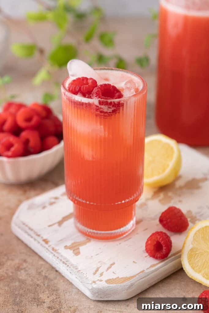 A tall glass of raspberry lemonade with ice and garnishes