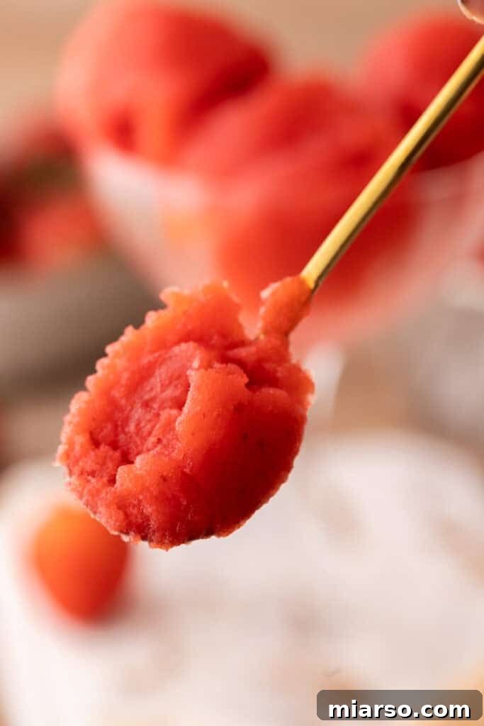 A hand scooping fresh strawberry sorbet from a container, showcasing its smooth texture.