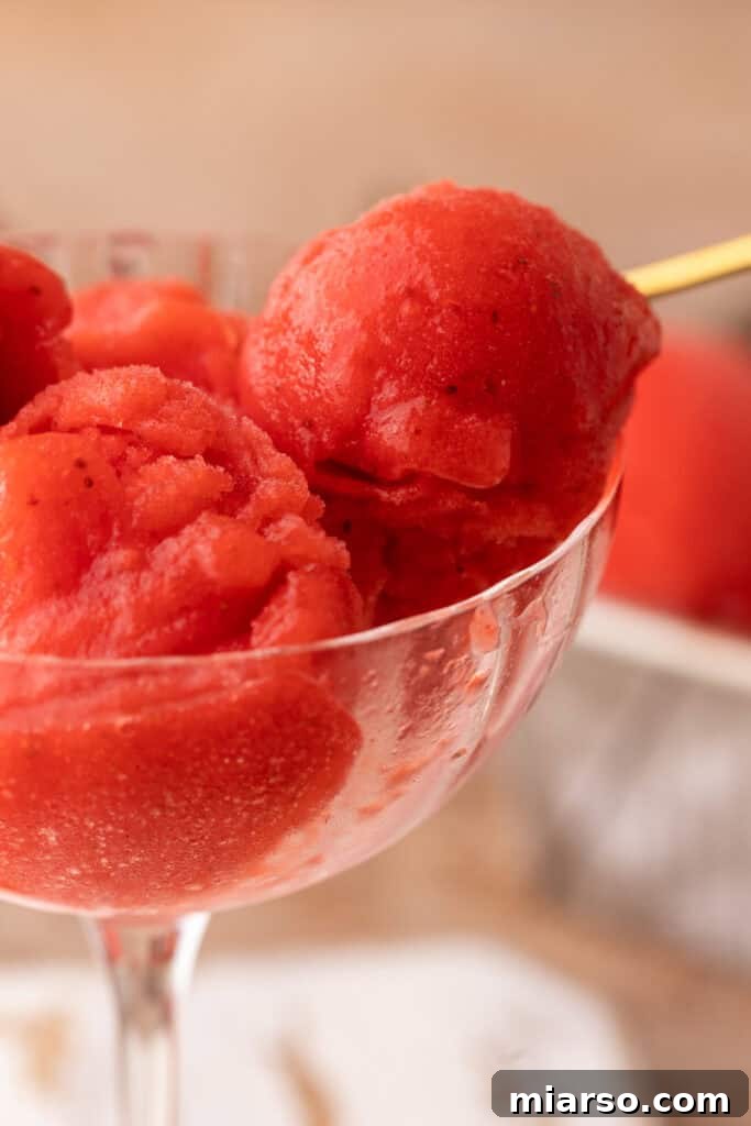 A tall glass filled with perfectly scooped homemade strawberry sorbet, garnished with a fresh strawberry.