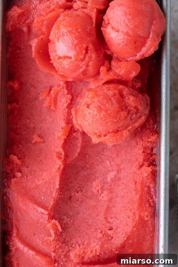 Firm, scoopable strawberry sorbet setting in a loaf pan, ready to be served.