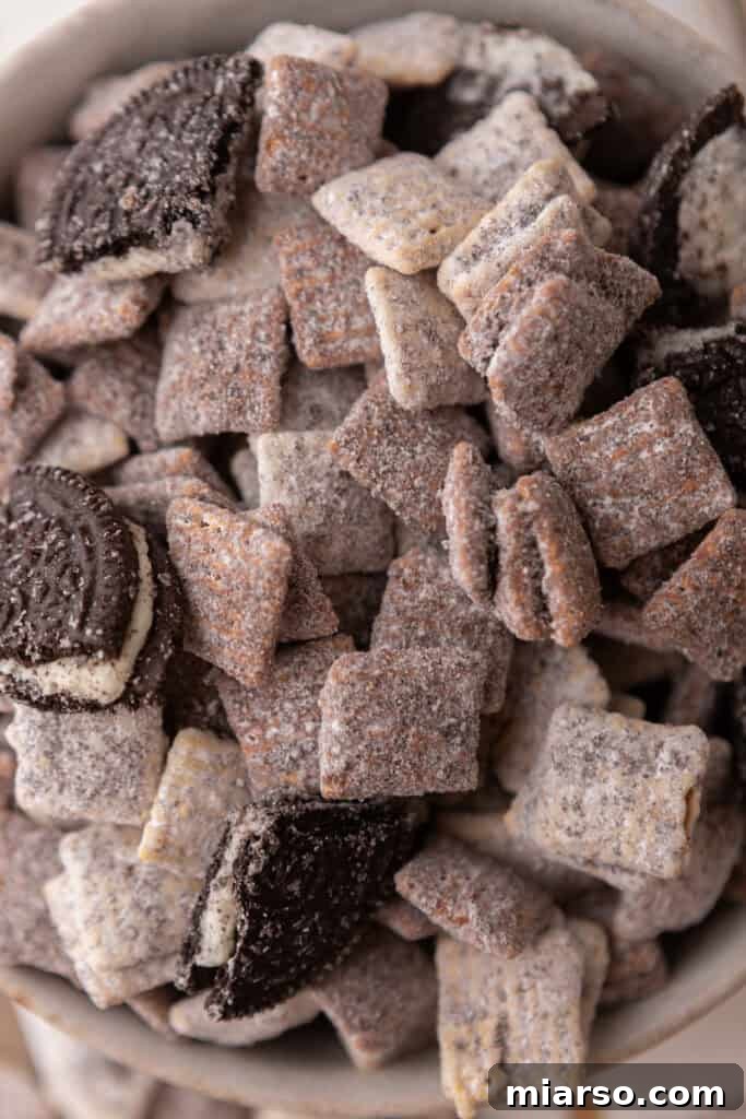 Close-up of freshly made Cookies and Cream Muddy Buddies, showcasing the crushed Oreos and chocolate coating on Chex cereal.