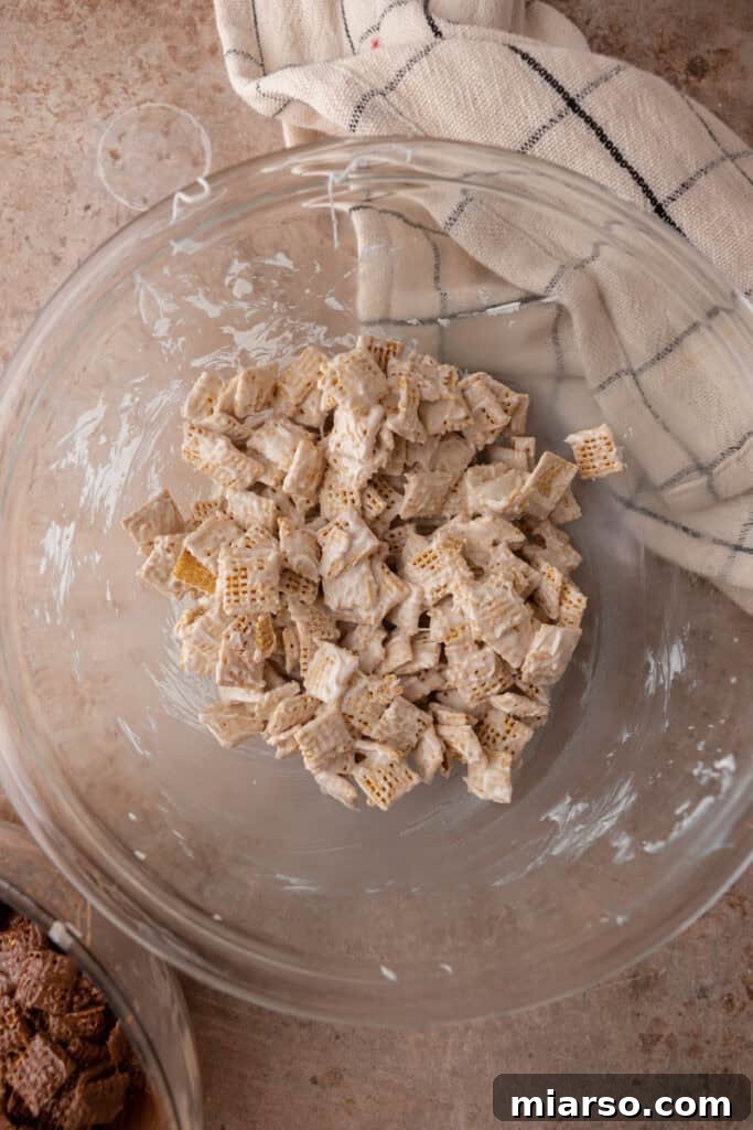 White chocolate chips being mixed with Chex cereal in a bowl with a spatula.