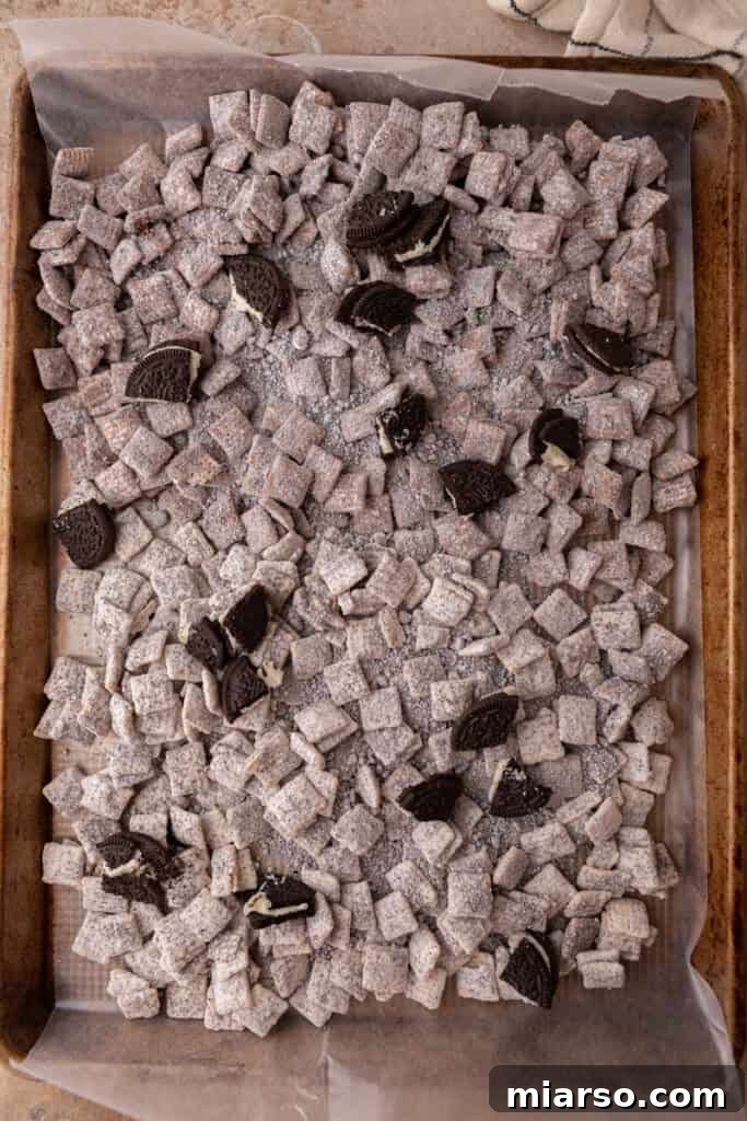 Fully mixed cookies and cream muddy buddies spread out on a parchment-lined baking sheet.