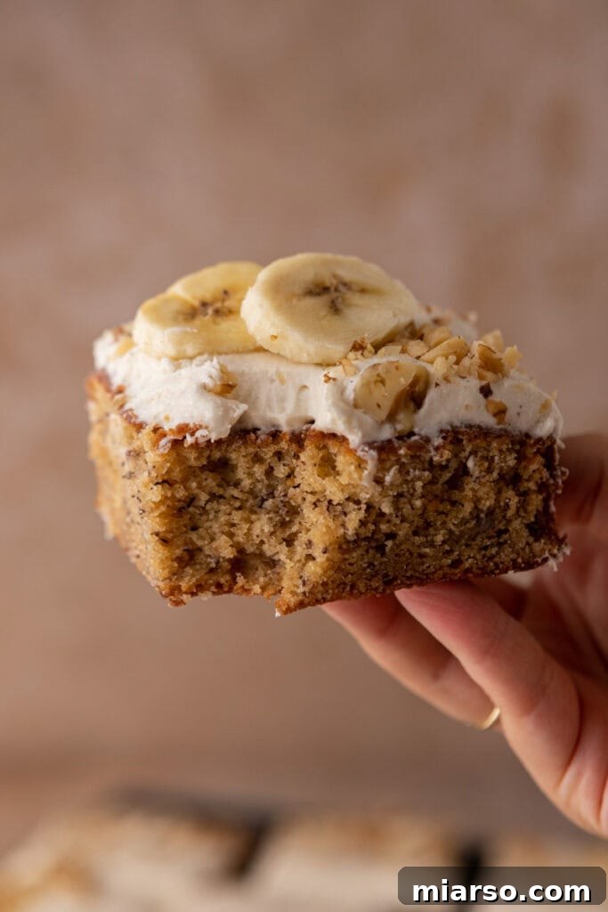 Simply Irresistible Banana Cake 4 A hand holding up a slice of the banana cake recipe, showcasing its moist texture and rich frosting