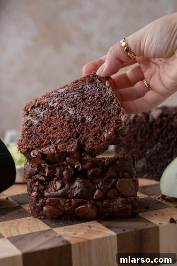 Decadent Double Chocolate Zucchini Loaf 13 A hand reaching for a slice of warm Double Chocolate Zucchini Bread, highlighting its appealing texture