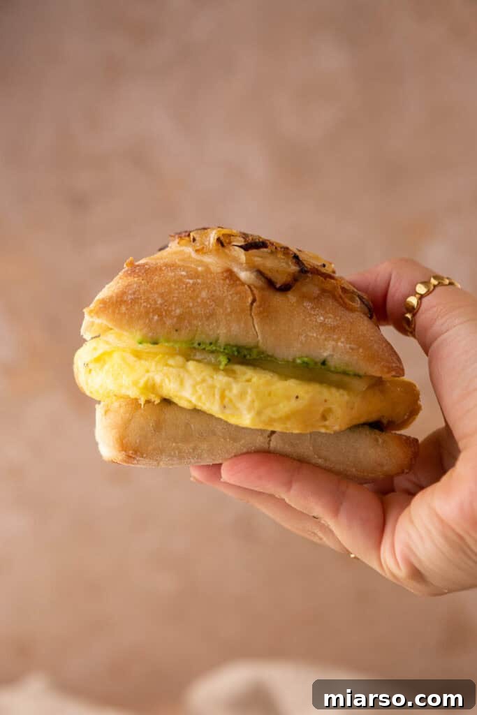 A person holding a delicious Starbucks Egg Kale Pesto Mozzarella Sandwich copycat recipe, ready to take a bite, highlighting its homemade appeal.