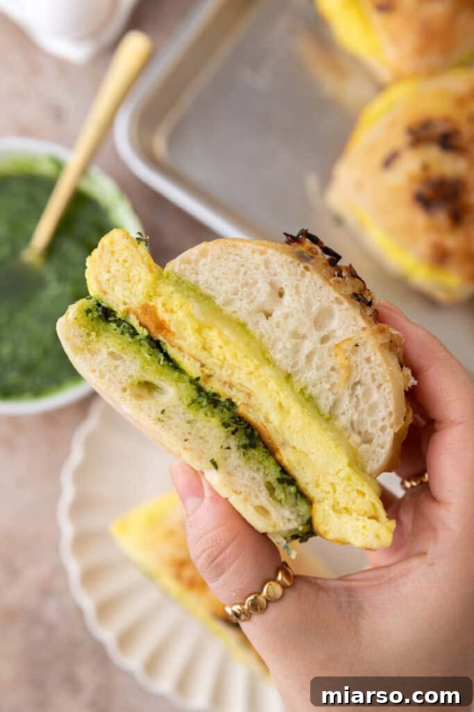 A close-up of a hand holding a Starbucks Egg Kale Pesto Mozzarella Sandwich copycat, highlighting the fresh ingredients and golden-brown bun.