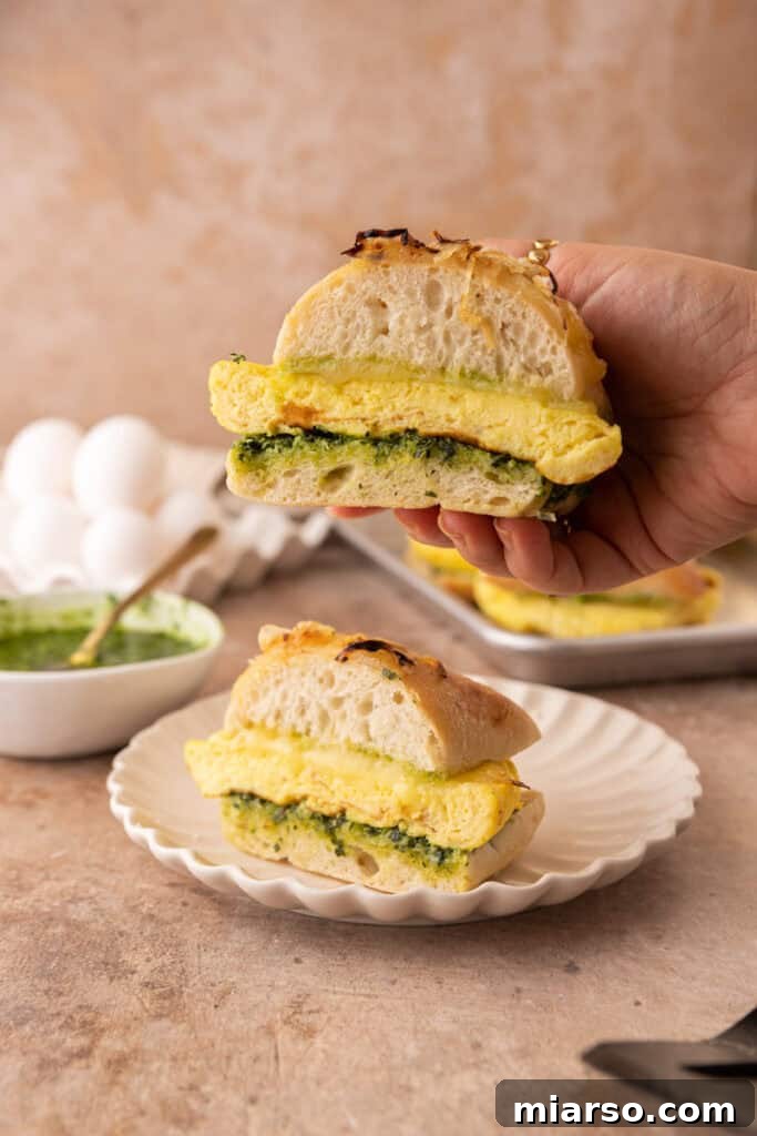 A hand holding a freshly assembled Starbucks Egg Kale Pesto Mozzarella Sandwich copycat recipe, showing off its delicious layers.