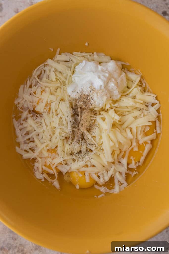 Raw egg mixture in a bowl with shredded cheeses and seasonings, prepared for making the fluffy egg patties for the Starbucks sandwich.