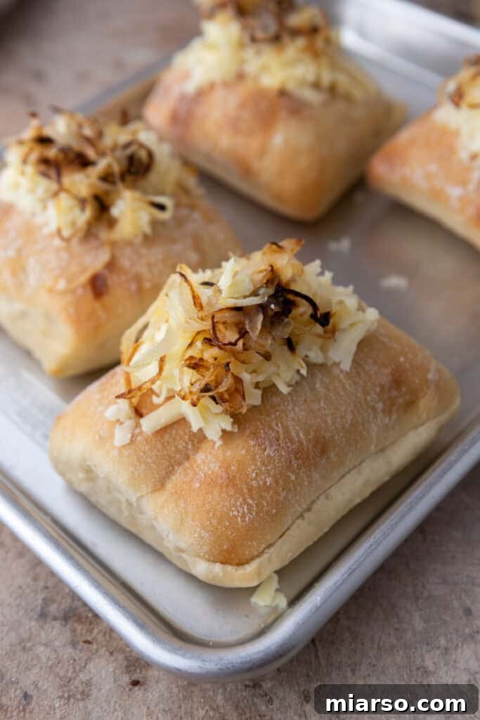 Ciabatta buns topped with caramelized onions and shredded cheddar cheese, ready for toasting in the oven for the Starbucks sandwich.