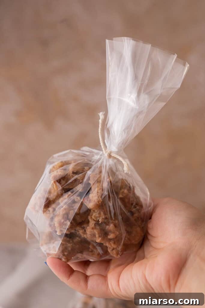 A hand holds a single New Orleans pecan praline, elegantly wrapped in a clear bag with a string, suggesting it's a gift.