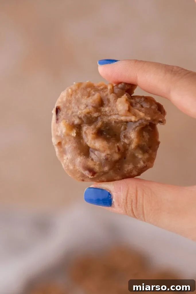 A hand holds up a finished, soft New Orleans praline patty, showing its creamy texture and embedded pecans.