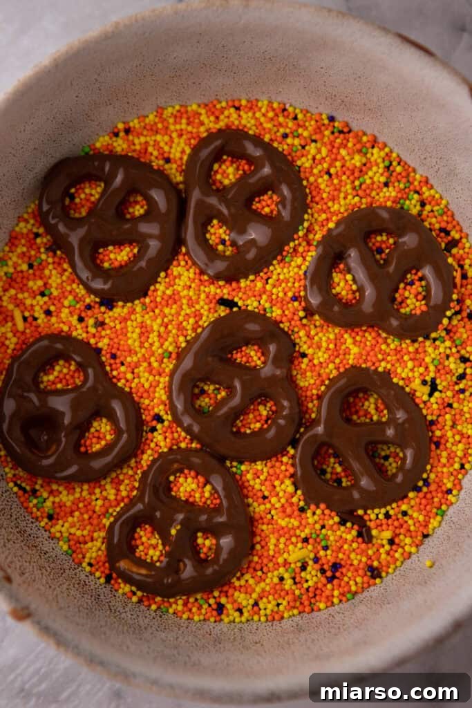 Sweet and Salty Chocolate Pretzel Delight 7 A chocolate-covered pretzel being decorated with colorful sprinkles.