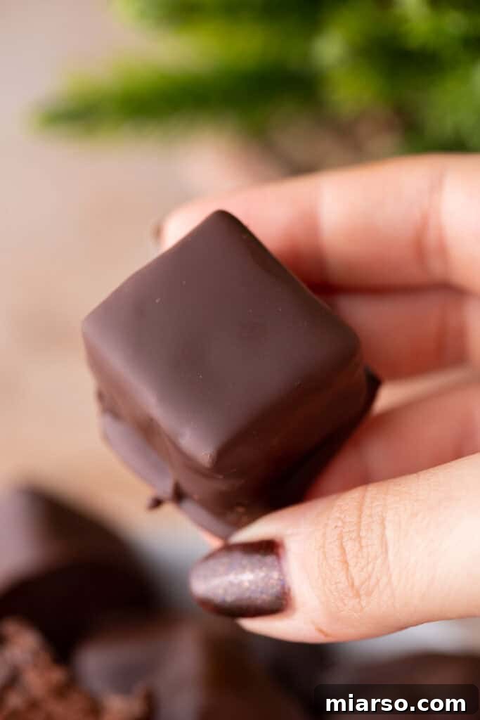 Effortless Three Musketeers Cool Whip Treats 4 A hand holding a freshly dipped chocolate candy square with a smooth coating.