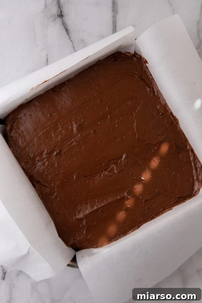 Effortless Three Musketeers Cool Whip Treats 8 Chocolate candy filling spread evenly in a parchment-lined square baking dish before freezing.