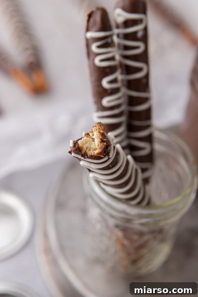 Decadent Caramel Chocolate Pretzel Rods 11 An inviting close-up of three caramel chocolate covered pretzel rods, glistening with melted chocolate and sprinkled with sea salt, standing upright in a small cup.
