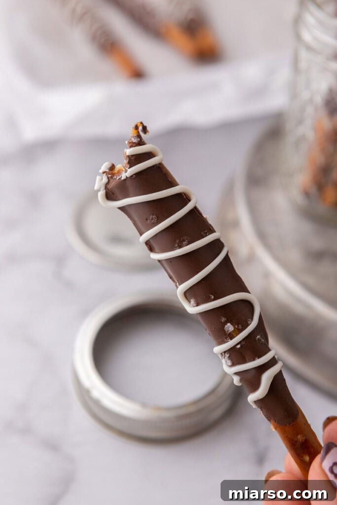 Decadent Caramel Chocolate Pretzel Rods 13 A single, perfectly crafted caramel chocolate covered pretzel rod, adorned with flaky sea salt, held delicately to showcase its delicious layers.