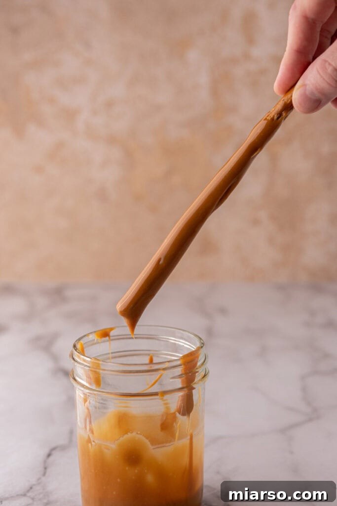 Decadent Caramel Chocolate Pretzel Rods 7 A pretzel rod being carefully dipped into a rich, melted caramel mixture, ensuring an even and generous coating.