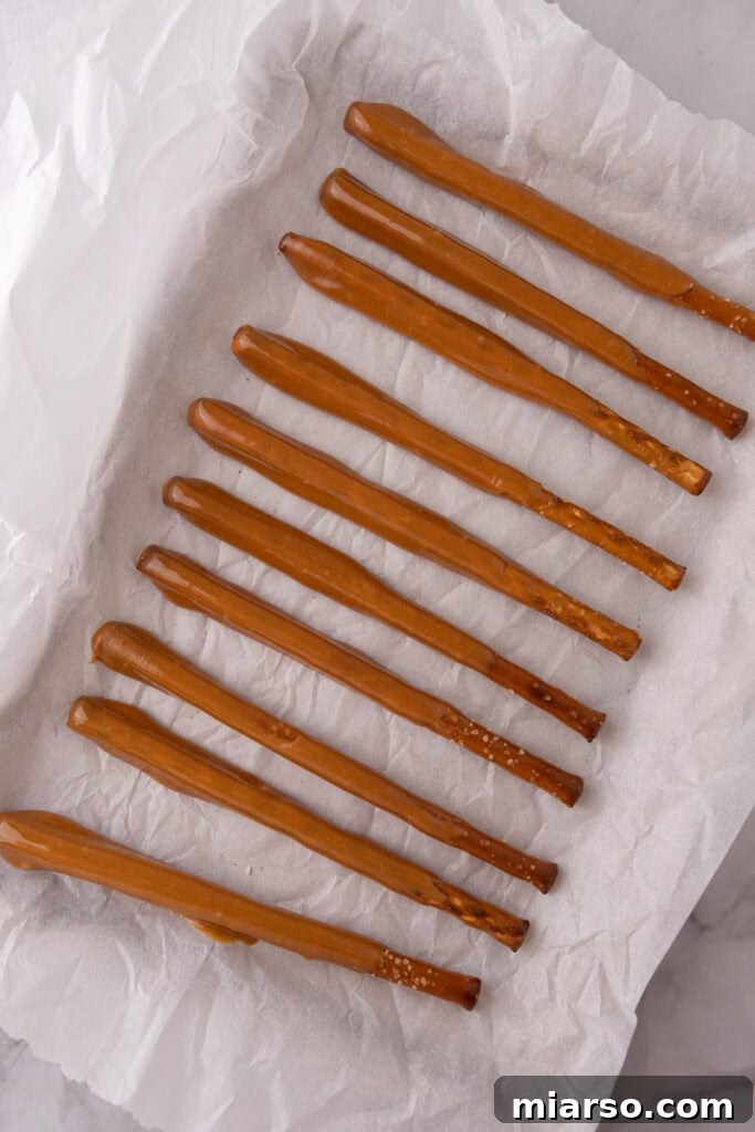 Decadent Caramel Chocolate Pretzel Rods 8 Caramel-coated pretzel rods neatly arranged on a baking sheet lined with parchment paper, allowing the caramel to set.
