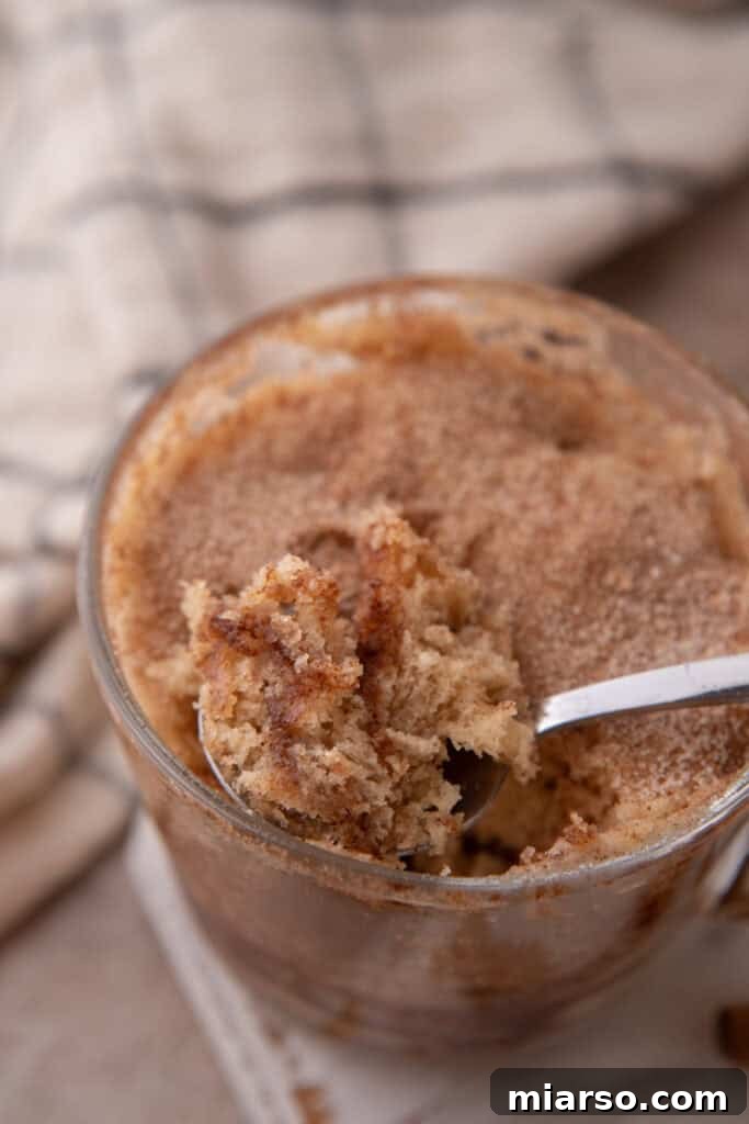 Snickerdoodle mug cake recipe in a cup getting scooped, showing its soft texture and cinnamon swirl