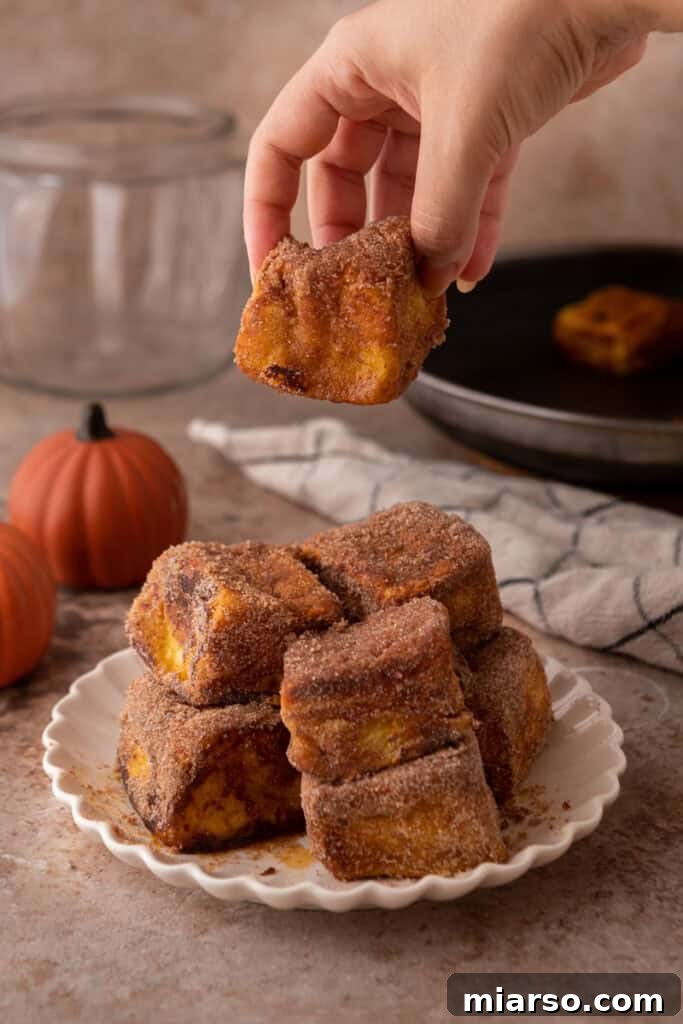 A hand gently placing a warm Hawaiian Roll Pumpkin French Toast bite onto a pristine white plate.