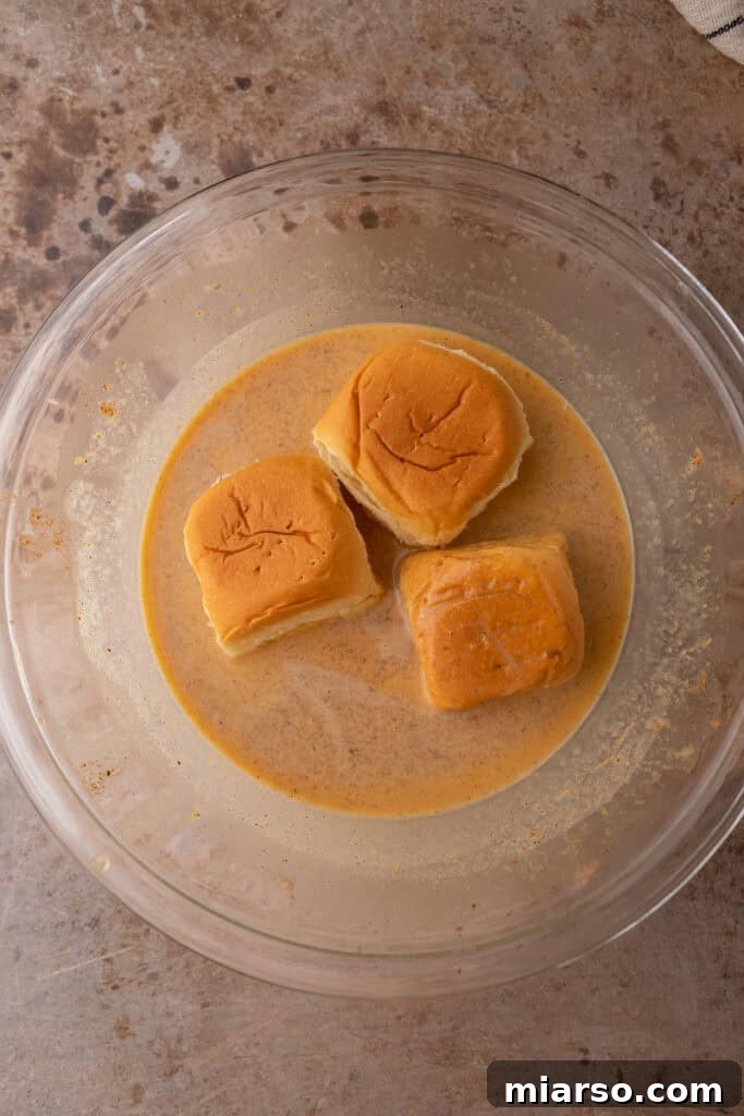 Hawaiian sweet rolls soaking in a rich pumpkin custard mixture, ready for cooking.
