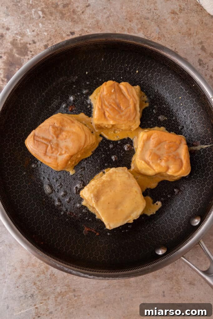 Hawaiian rolls dipped in pumpkin custard cooking on a hot skillet, achieving a golden brown color.