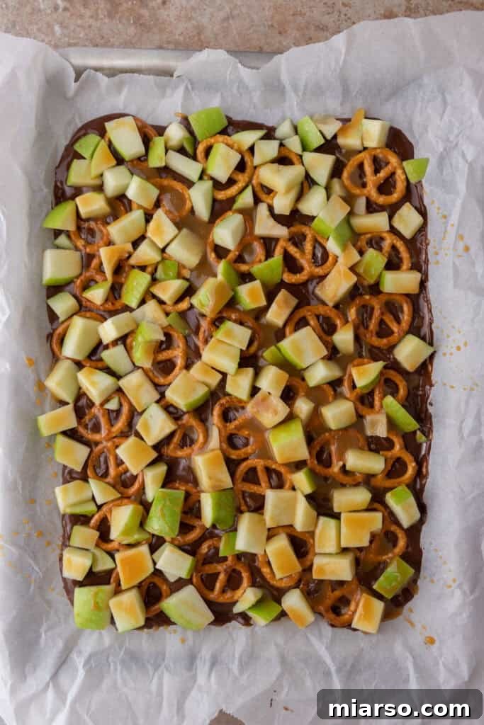 The Ultimate Caramel Apple Bark Recipe 7 pretzels and other ingredients on top of the chocolate