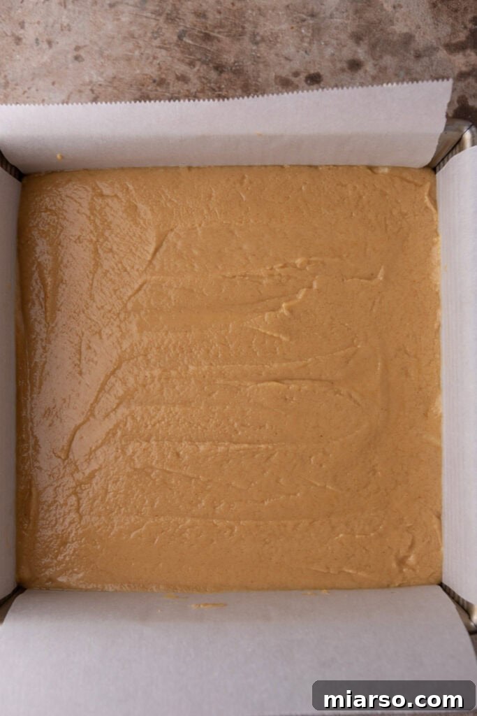 Effortless Microwave Peanut Butter Fudge 8 The smooth peanut butter fudge mixture spread evenly in a parchment-lined pan, chilling in the refrigerator.