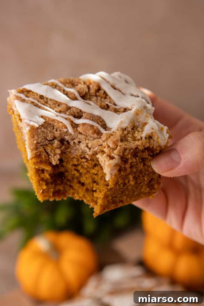 A delicious slice of moist pumpkin coffee cake with streusel topping, held by a hand, ready to be enjoyed.