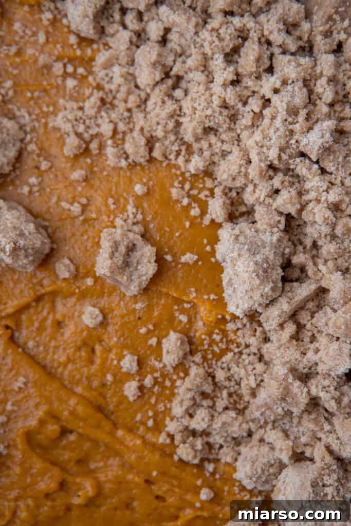 The delightful streusel topping being sprinkled generously over the pumpkin cake batter.