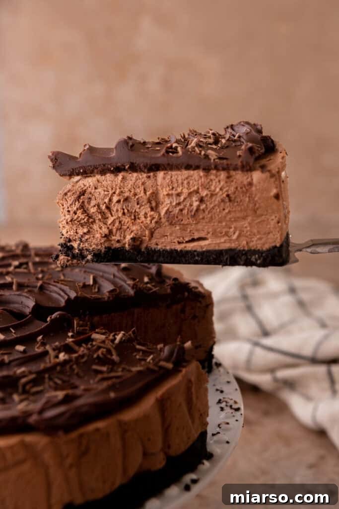 A generous slice taken out of a whole no-bake chocolate cheesecake, revealing its creamy layers and a thick Oreo crust, garnished with chocolate curls.