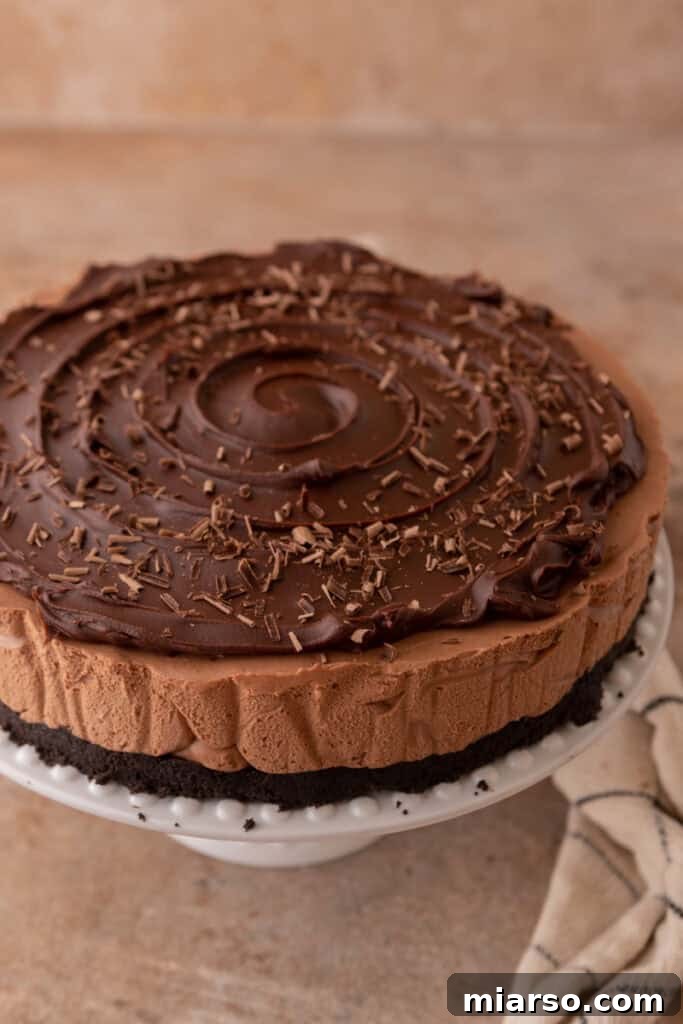 An offset spatula smoothing the ganache topping over the no-bake chocolate cheesecake for an even finish.