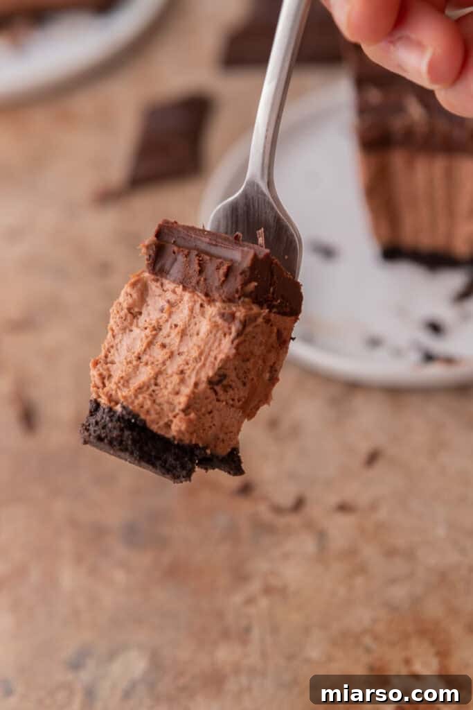 A fork taking a bite from a slice of no-bake chocolate cheesecake, showing the rich, creamy texture.