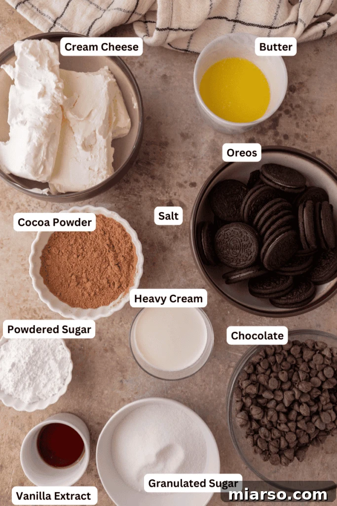 A collection of ingredients laid out for a no-bake chocolate cheesecake recipe, including cream cheese, chocolate chips, cocoa powder, heavy cream, Oreos, and butter.