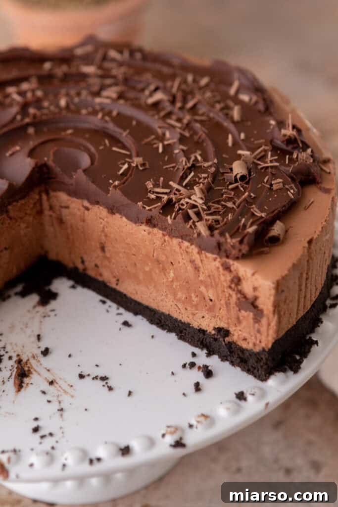 A freshly sliced no-bake chocolate cheesecake, showing off its distinct layers of Oreo crust, creamy chocolate filling, and glossy ganache topping.