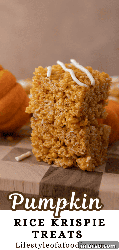 Tall stack of Pumpkin Rice Krispie Treats with a rich orange color and white chocolate drizzle.