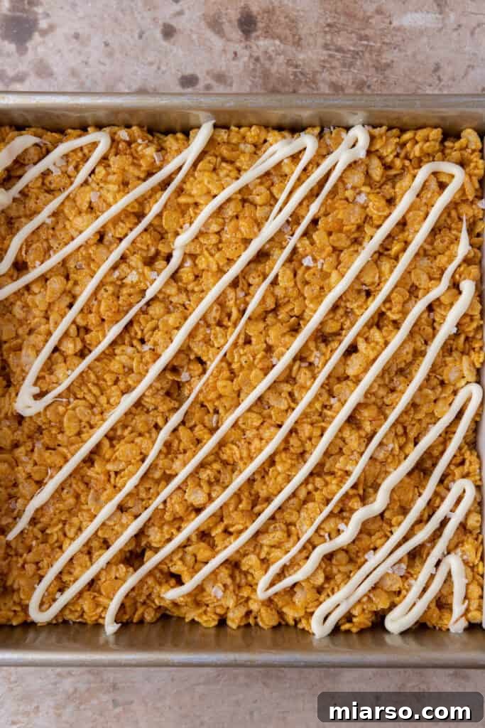 Finished pumpkin Rice Krispie treats in a pan with white chocolate drizzle.
