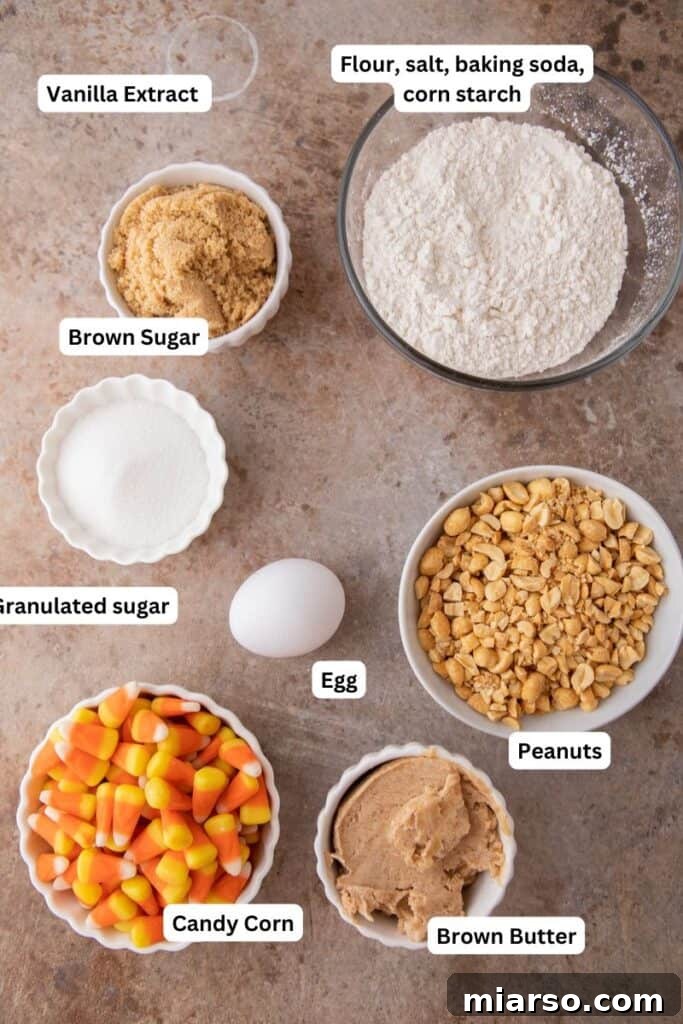 Assortment of ingredients laid out for candy corn cookies recipe, including butter, sugars, eggs, flour, peanuts, and candy corn.