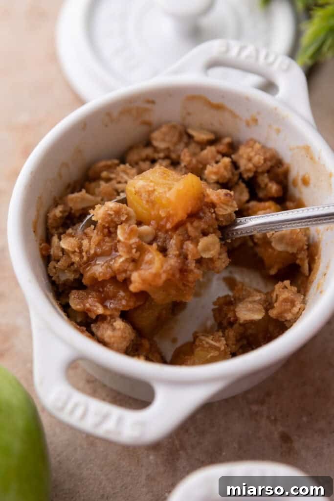 A close-up of a Microwave Apple Crisp for One in a mug, with a spoon digging into the warm, bubbly goodness.